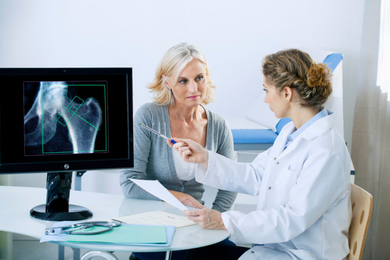 woman and doctor completing a osteoporosis diagnosis in the doctors office pointing to xray